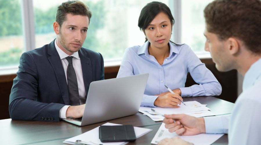 Three professionals discussing documents at an office table with a laptop.