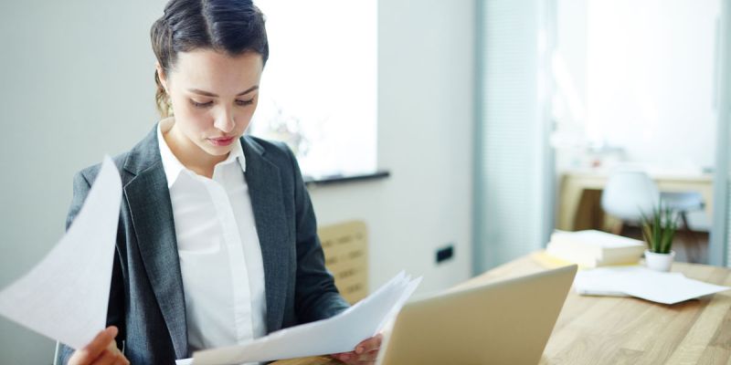 A Businesswoman in a suit sitting at a desk with papers.