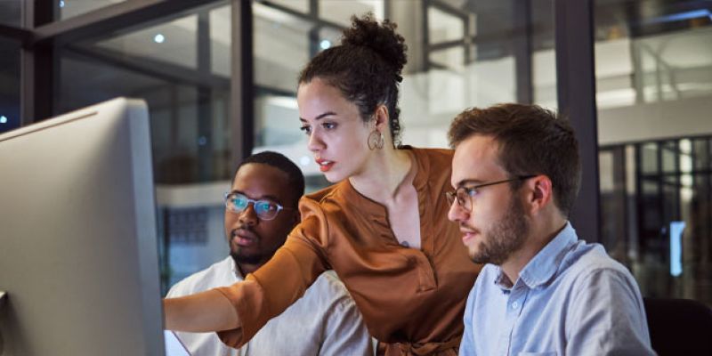 A female businesswoman pointing at a screen next to two coworkers.