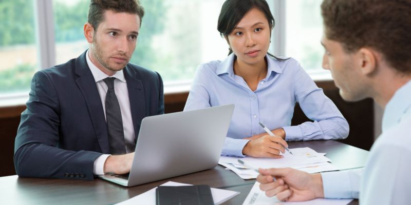 Three professionals discussing documents at an office table with a laptop.